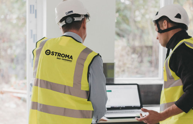 Two Stroma Built Environment engineers in hi-vis vests reviewing drawings on a laptop on site