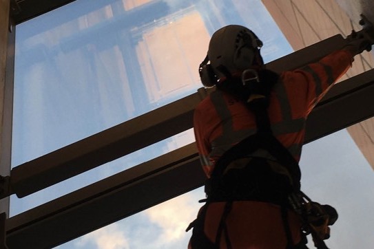 A Stroma rope access technician in orange PPE working on the underside of a building soffit
